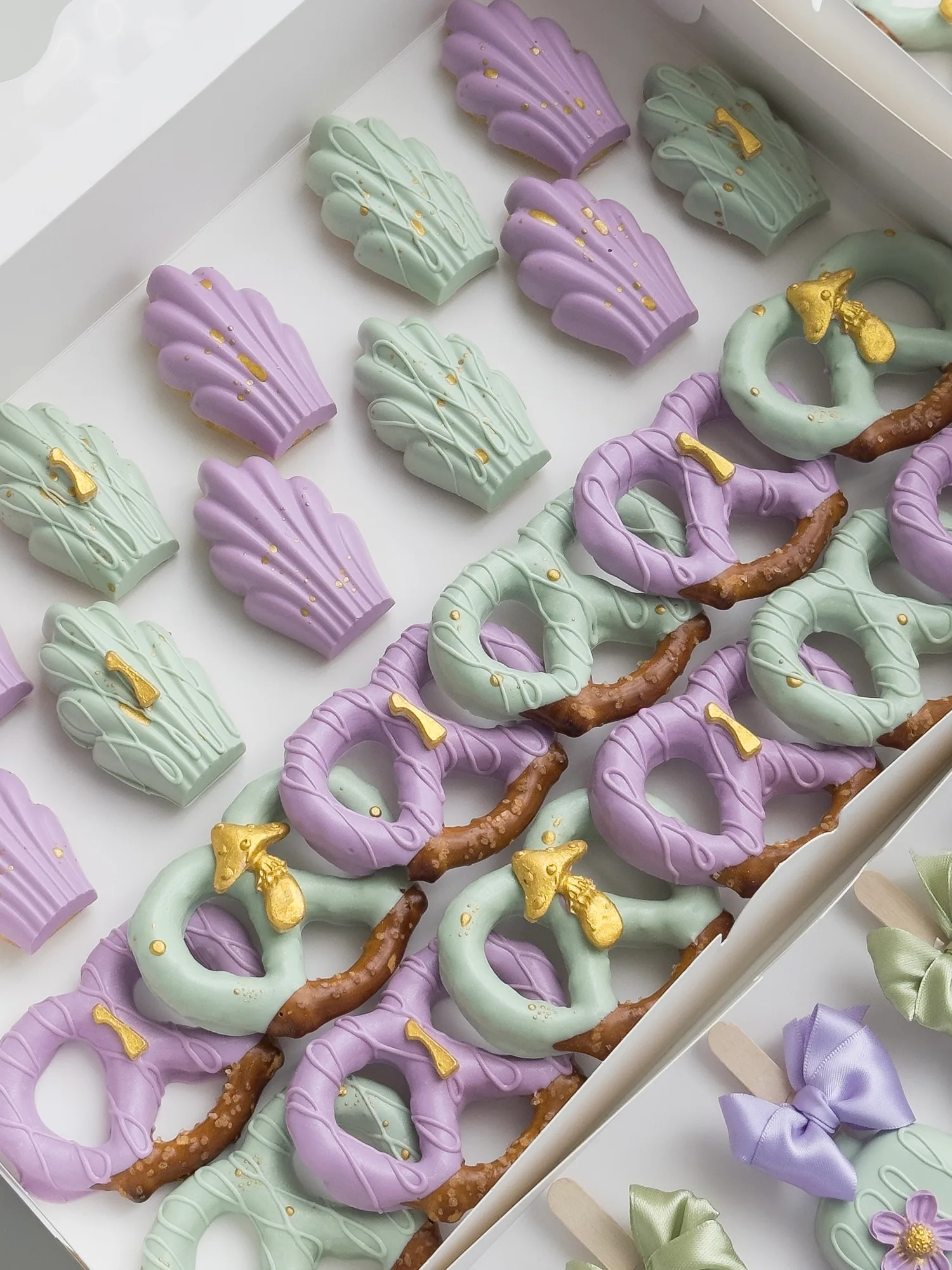 A white box of lavender and sage madeleines and dipped pretzels finished with gold bows.
